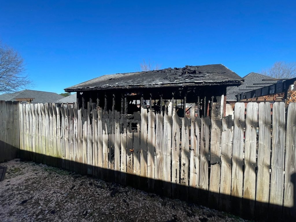 Fire-damaged outbuilding and fence between two homes
