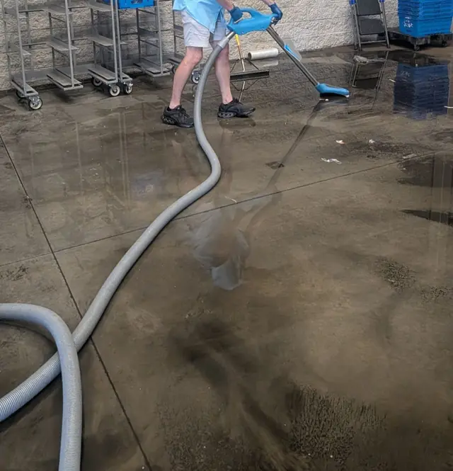 Technician extracting standing water from a commercial concrete floor with an extraction wand and hose